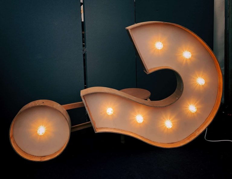 Large metal question mark sign with lightbulbs inside of it laying down sideways