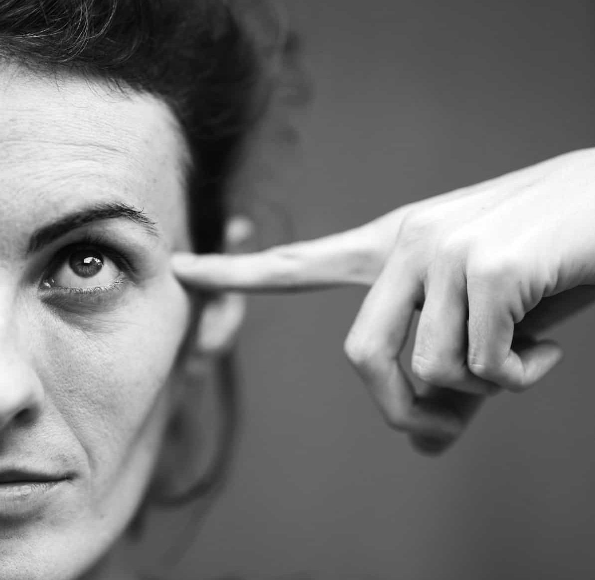 Pointer finger is pointing at the side of a persons head as their eyes look up