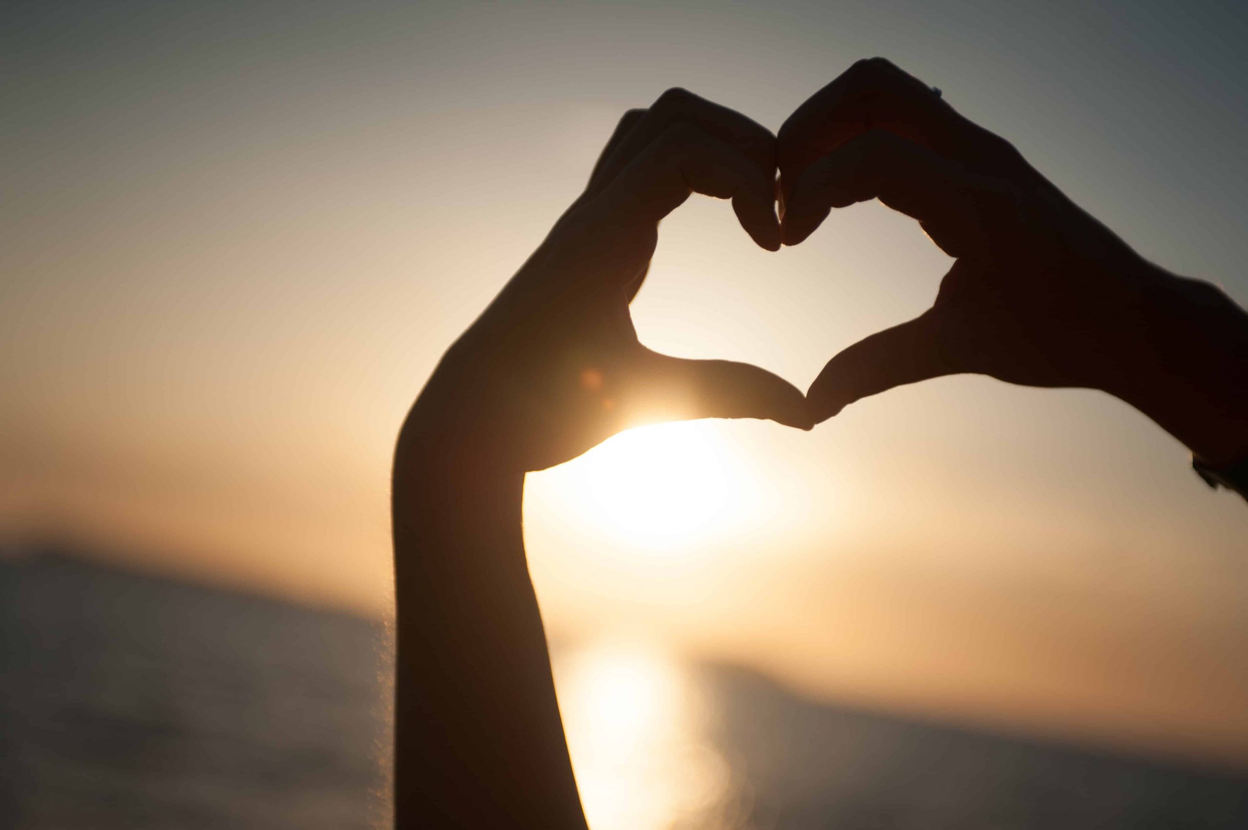 Person holding hands to form a heart against a water and sun background