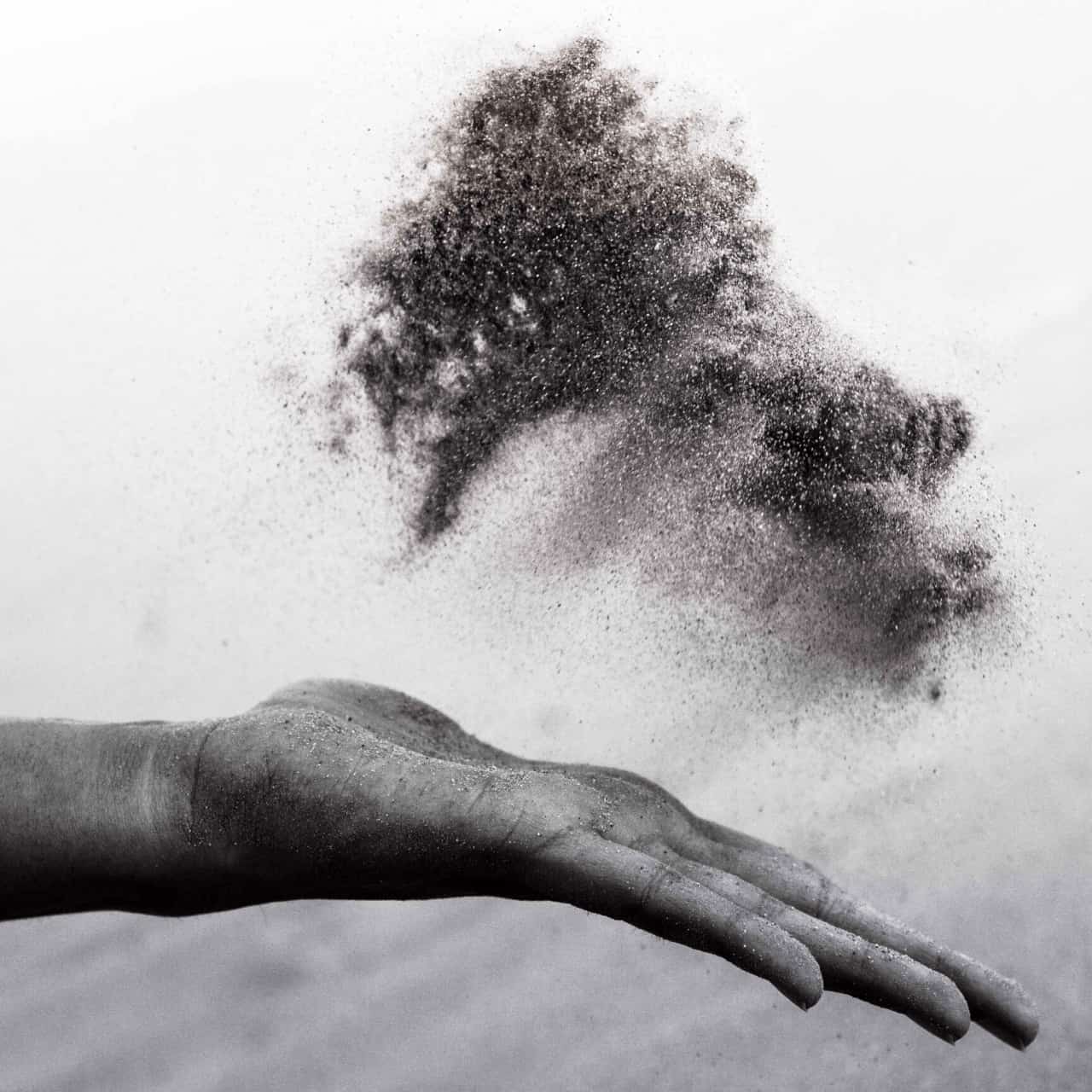 A picture of a hand throwing and letting go of sand/grain