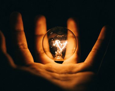 A small lit up lightbulb floating in someone's open hand