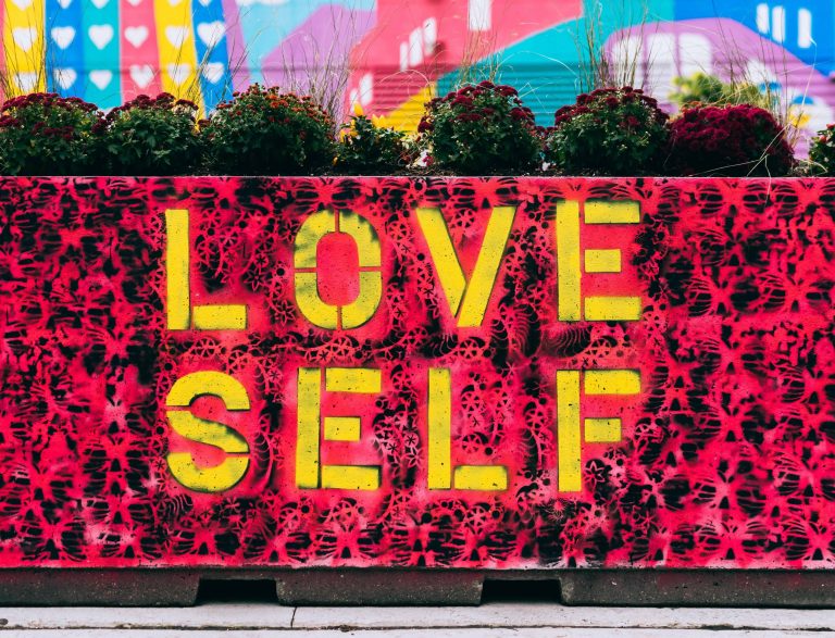 "Love Self" spray painted on a outdoor walkway wall with bright colors