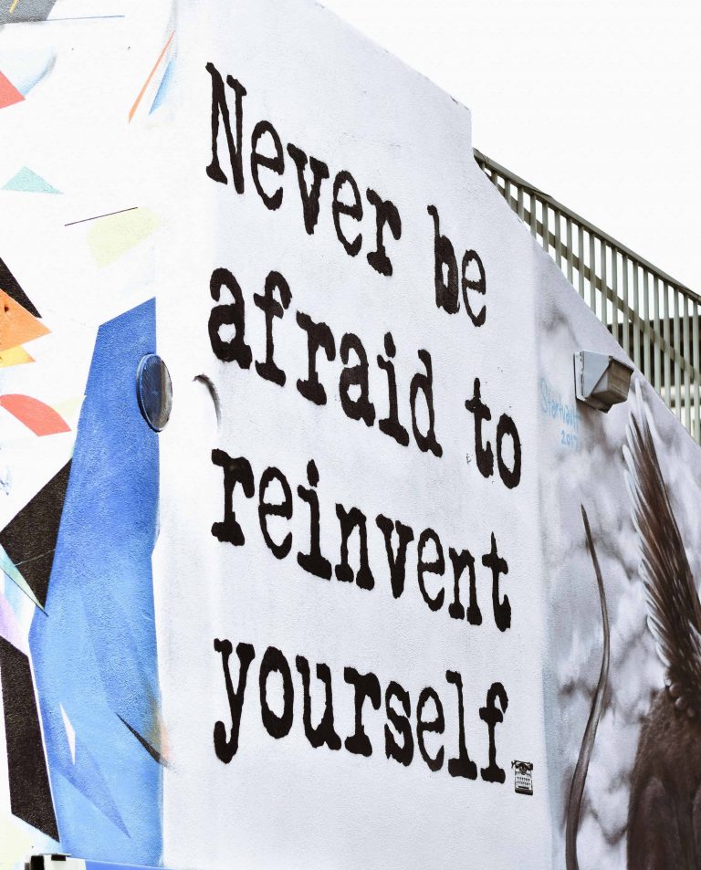 "Never be afraid to reinvent yourself" quote painted on the side of a building