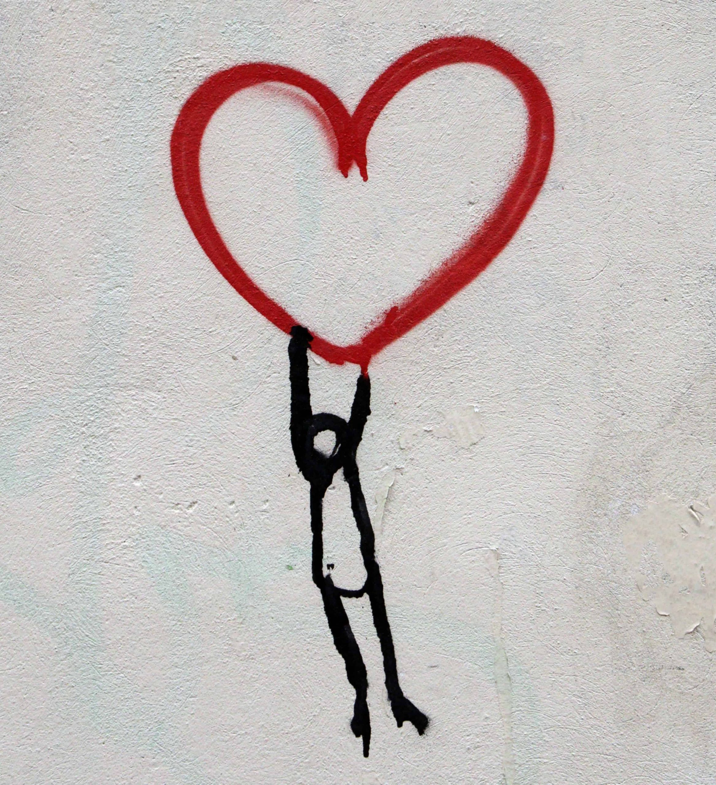 Painting on wall of stick figure holding a large red heart above its head