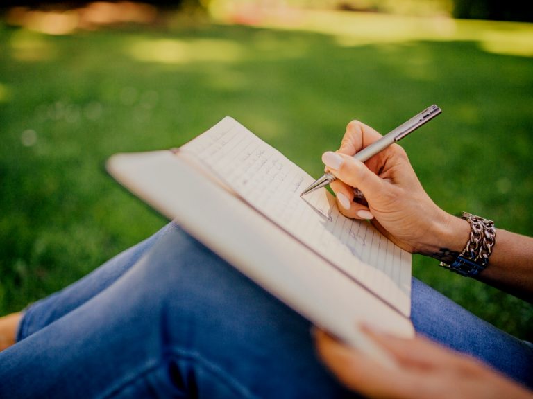 A woman sitting in the grass and writing in a journal