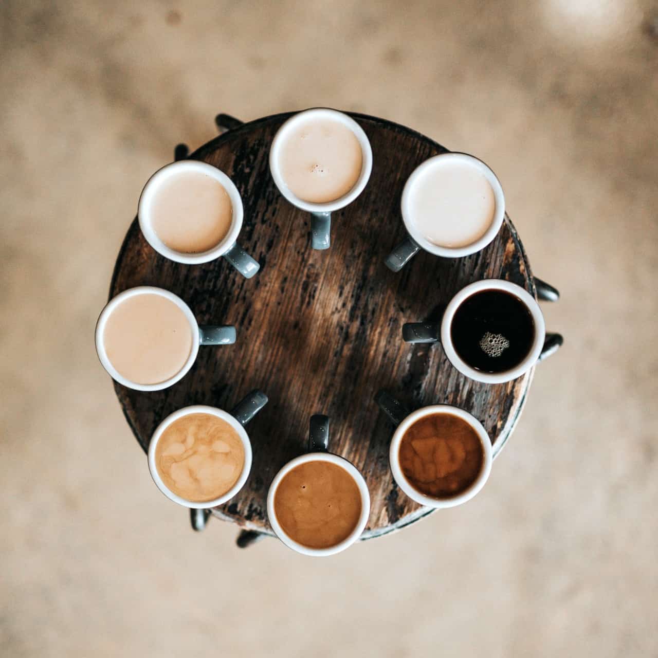 Looking down upon 8 cups of coffee of different shades in a circle around a wooden table
