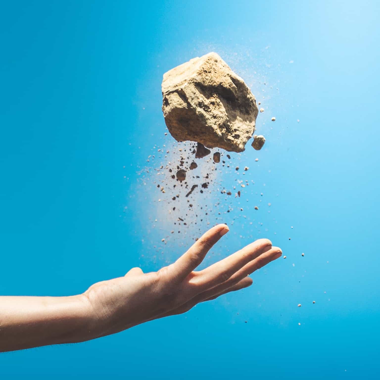 A hand throwing a large rock upward