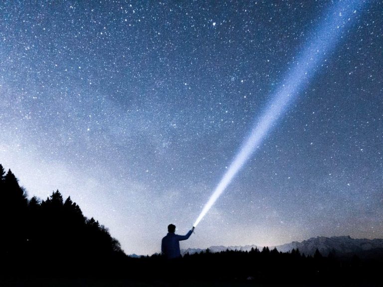 A person beaming a flashlight towards the starry night sky