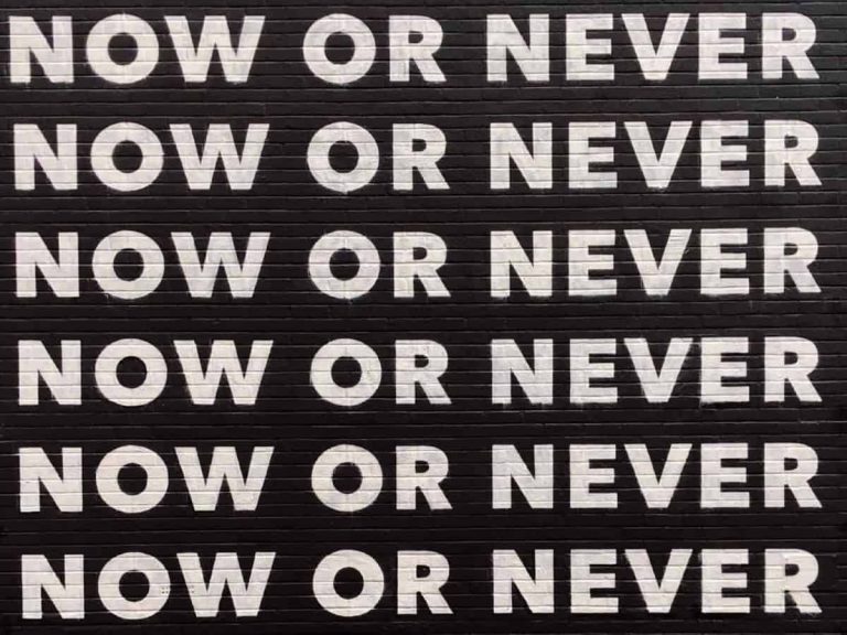 "Now or Never" painted quote on brick wall six times