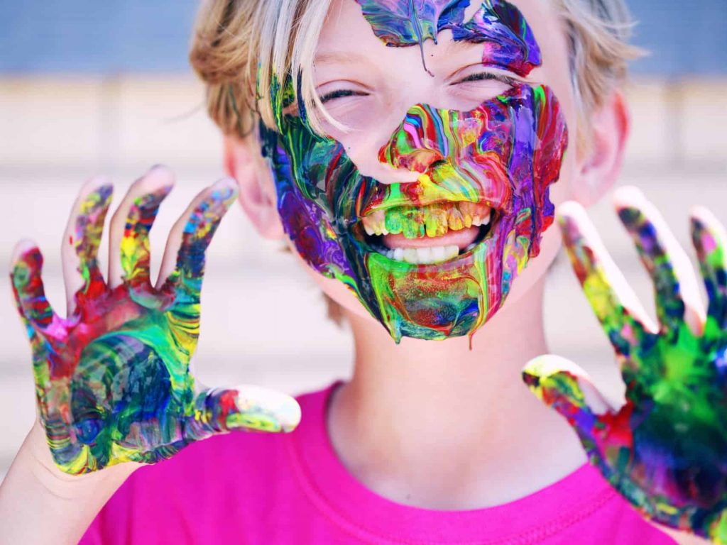 Kid with rainbow paint on hands and face
