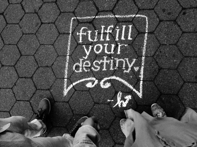 "Fulfill your destiny" quote written in chalk on the ground with 2 people looking down and their feet