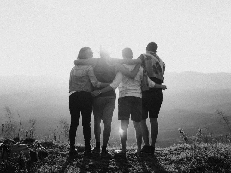 Four people in a group hug facing the sun