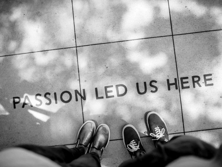 Two people looking down at the phrase "Passion led us here" written on the sidewalk