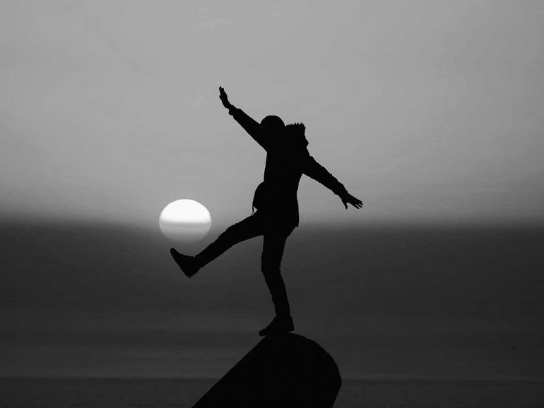 Person balancing on rock with sunset
