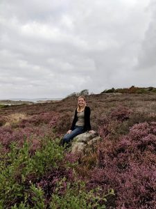 Kee sitting on a rock between purple and green flora