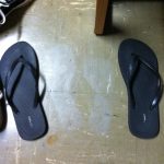 Grey ghost shoe prints on a tile floor next to flip flops