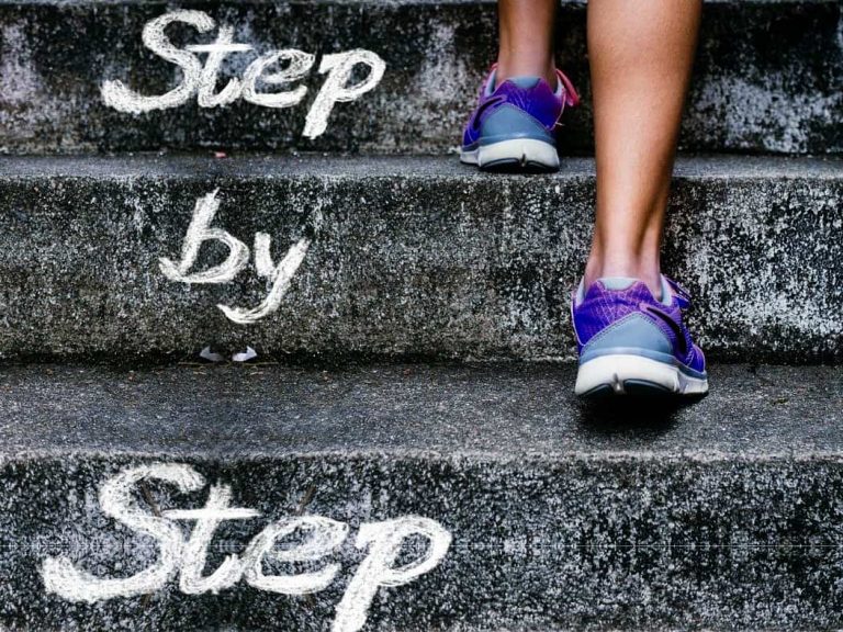 Person walking up stairs with the words, "Step by Step" written in chalk