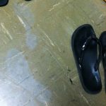 Grey ghost shoe prints on a tile floor next to flip flops