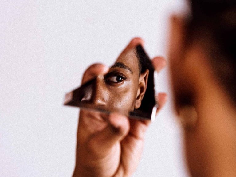 Person looking into a broken mirror piece at their reflection