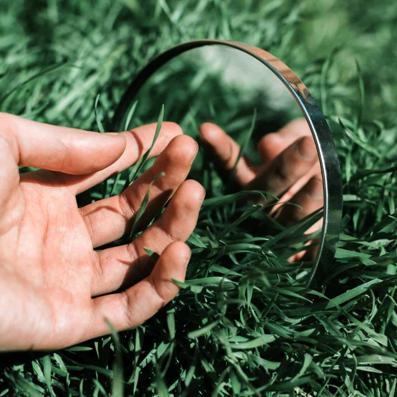 A hand reaching towards a mirror on the grass