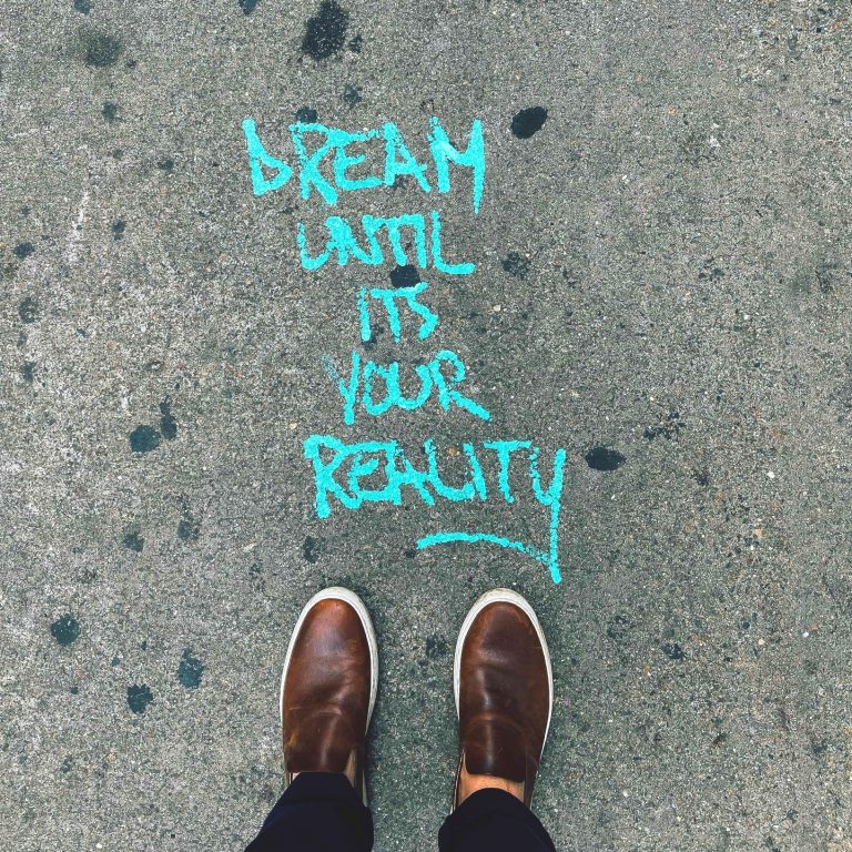A person standing on the sidewalk with "Dream until its your reality) written in front of their feet