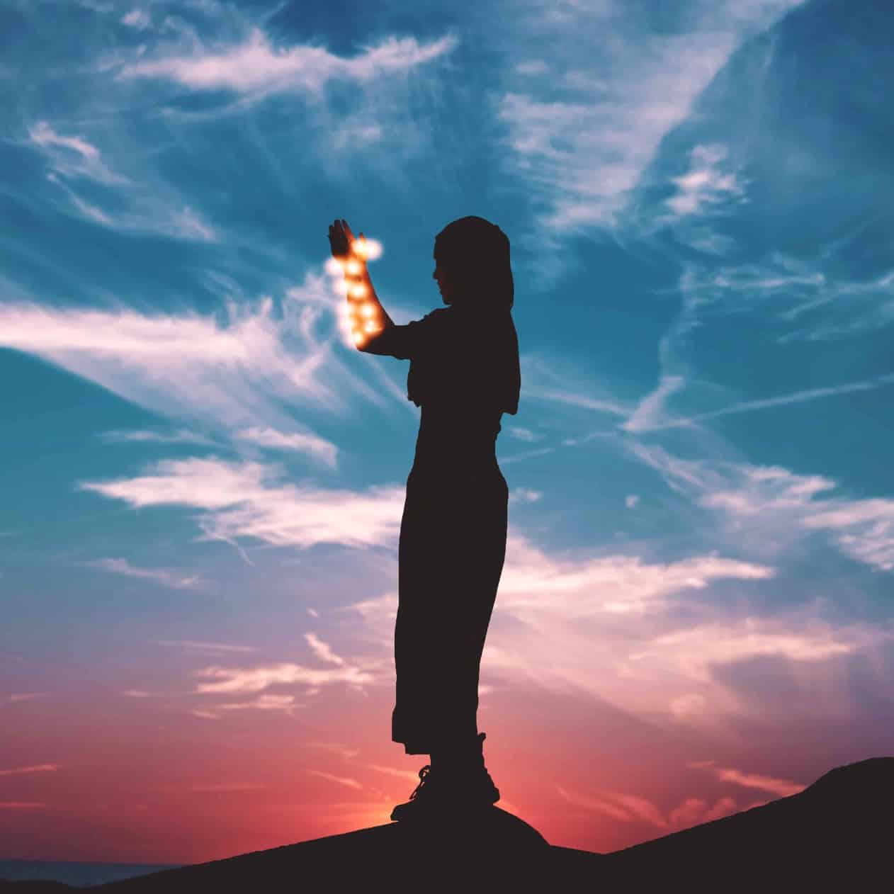 A person standing outside at sunset with lights wrapped around their arms