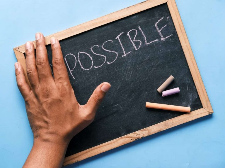 A chalkboard with a hand covering the "im" of "impossible"