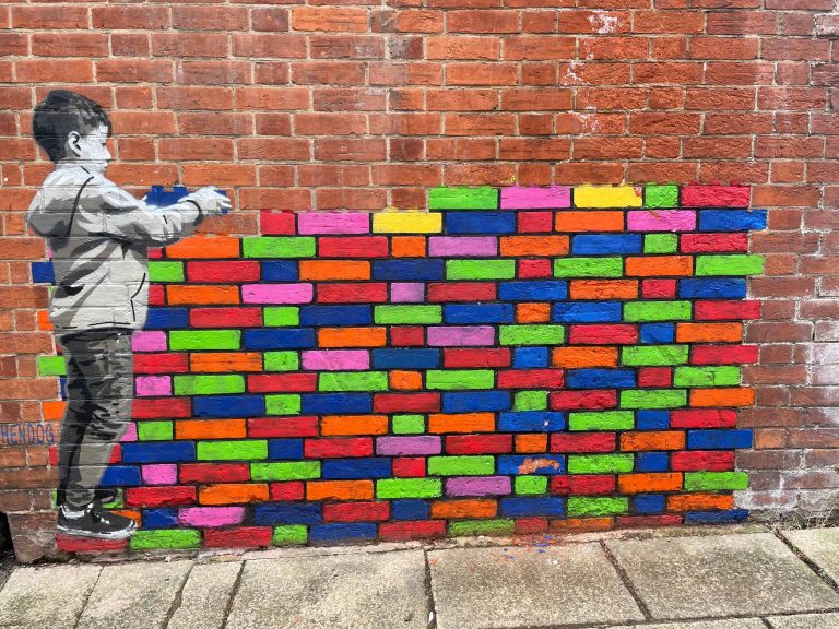 Street art on a brick wall of a boy stacking various colored bricks