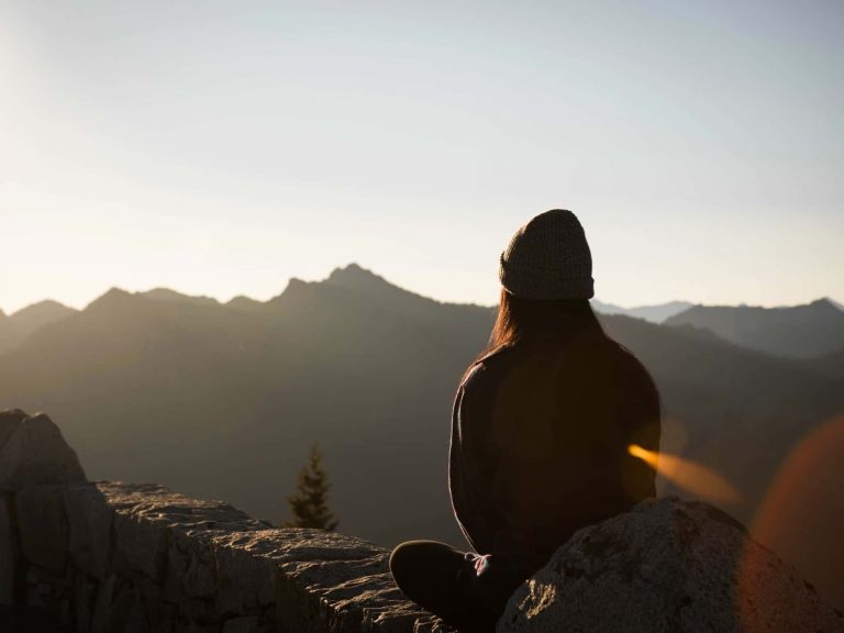 A person sitting still outside with the sunrise and rays
