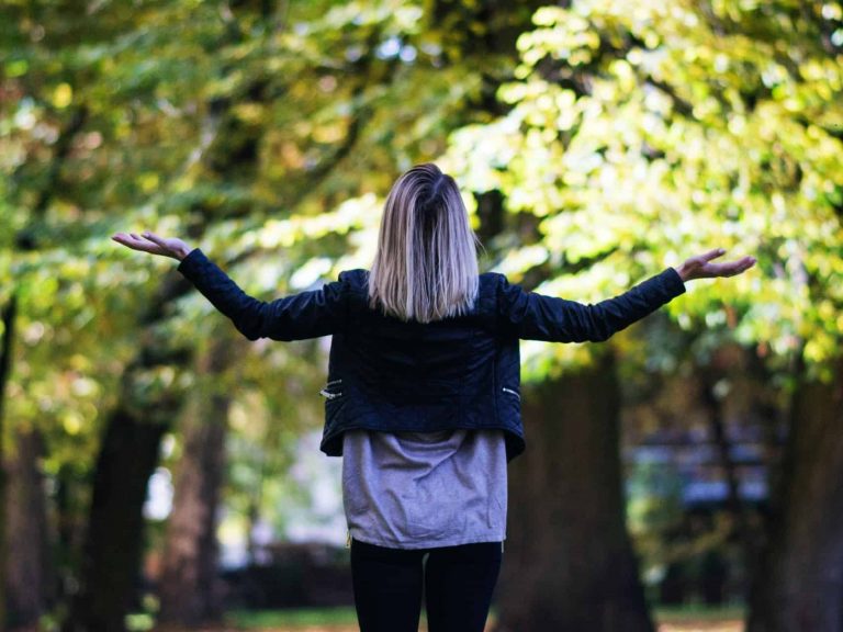 A woman outside with her hands/arms out like she's asking, "Why?"